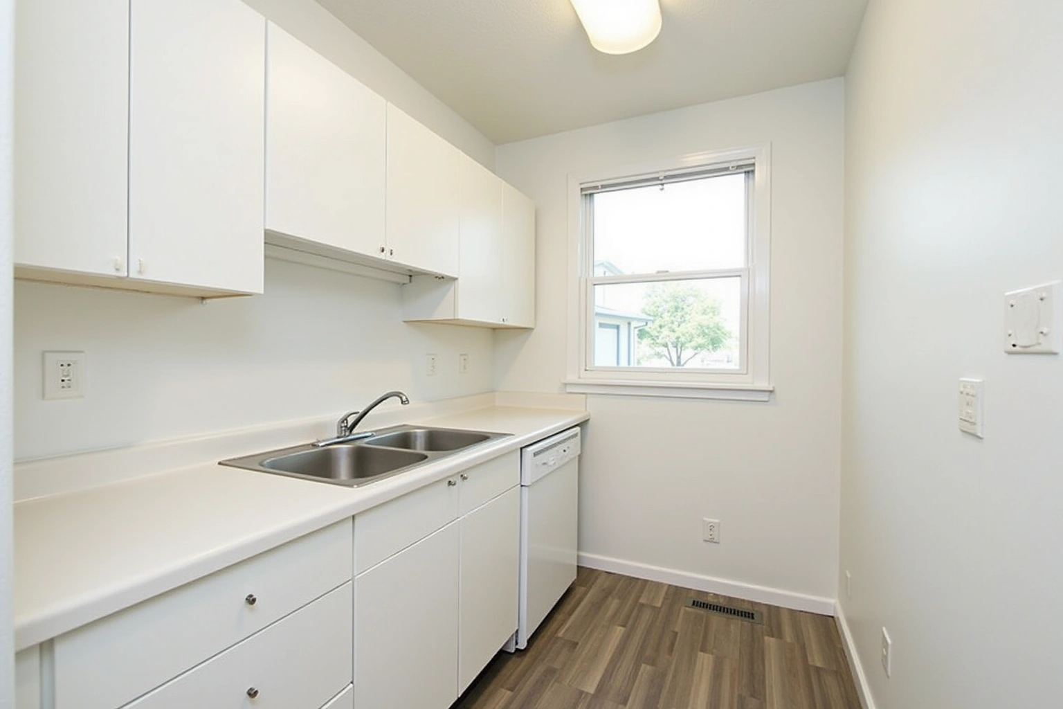 Small galley kitchen with white flat-panel cabinets, a cream laminate counter, a double sink and dishwasher by a window.