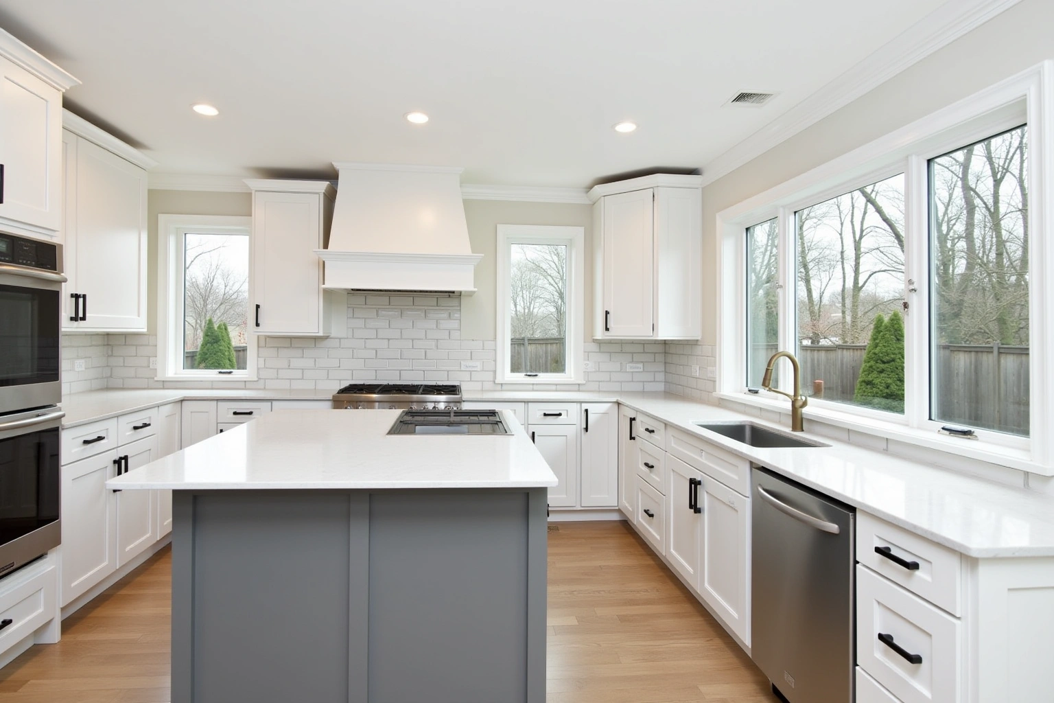 White shaker kitchen with matte black pulls, a grey island, subway tile and quartz counters, windows onto a fenced yard.