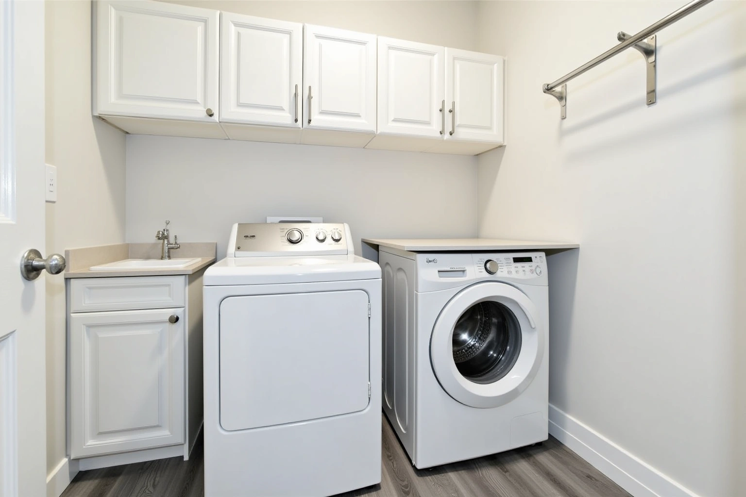 Laundry room with white raised-panel upper cabinets, a front-loading washer beside a dryer, a utility sink and hanging rod.