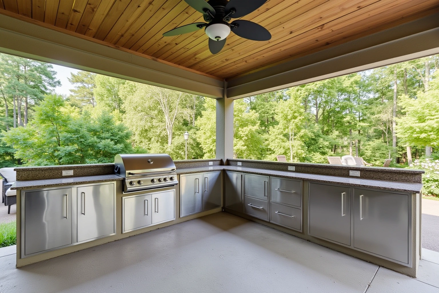 Covered patio outdoor kitchen with stainless steel doors and drawers under a granite counter, a built-in grill and ceiling fan.